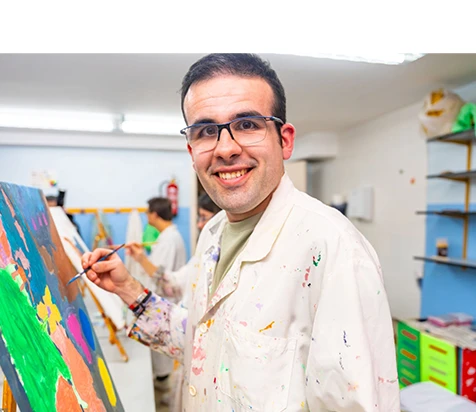 Joven con discapacidad sonriendo mientras pinta un lienzo.